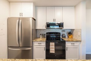 Eine Küche mit Edelstahlkühlschrank, einer Mikrowelle, einem Backofen und einer Arbeitsplatte aus Granit.
