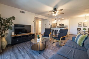Ein Wohnzimmer mit Flachbildfernseher, Deckenventilator und Essbereich mit Barhocker.