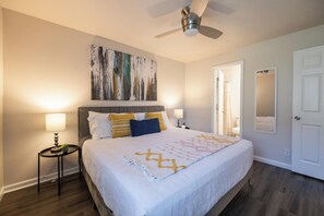 Ein Schlafzimmer mit Bett, Nachttischlampen, Deckenventilator, einem Gemälde und einer Tür.