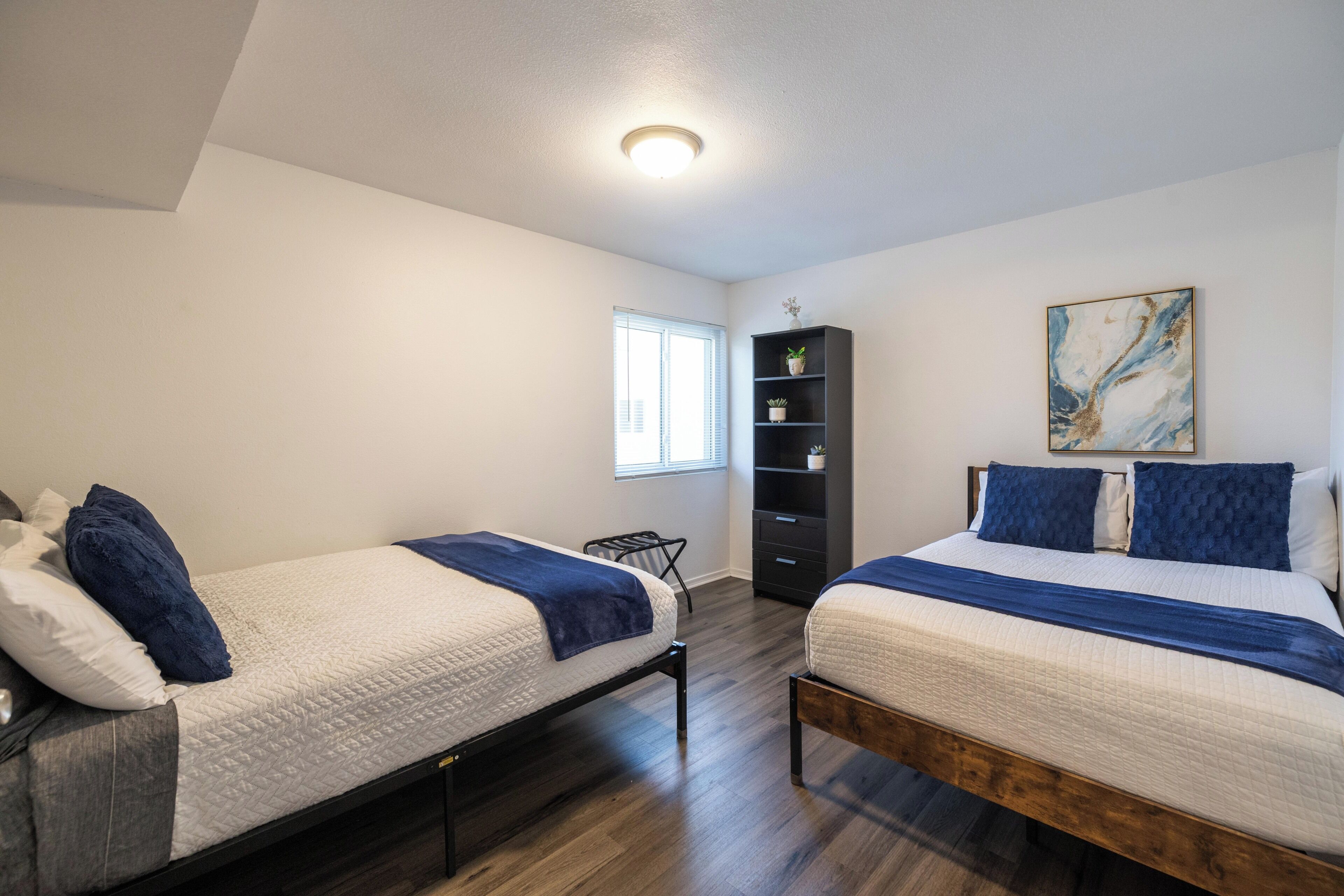A bedroom with two beds, a bookshelf, and a painting on the wall.