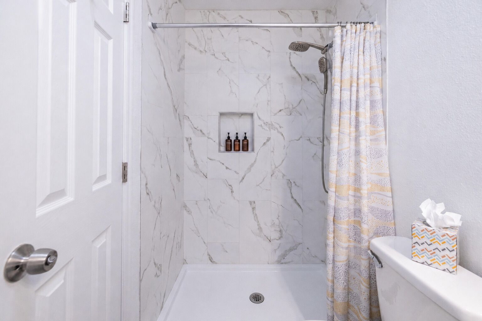 A bathroom with a shower, a toilet, and a shelf with toiletries.