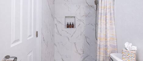 A bathroom with a shower, a toilet, and a shelf with toiletries.