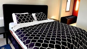 Un dormitorio con colcha de cuadros blancos y negros, dos lámparas de noche, una mesita y una ventana con vistas al exterior.