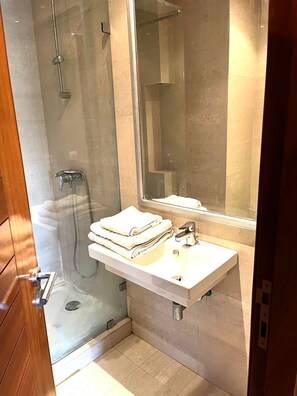 Un baño moderno con ducha de vidrio, un lavamanos blanco con espejo y toallas ordenadas.
