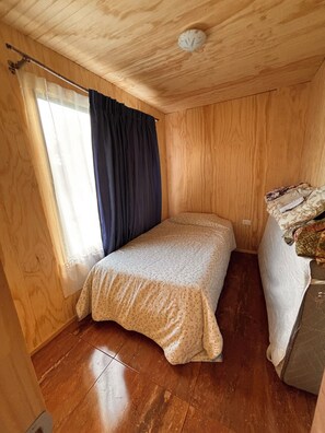 Ein kleines Zimmer mit einem Einzelbett, Holzwänden und einer schrägen Decke.