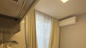 Ein kompaktes Hotelzimmer mit Küchenzeile, einem Bett, einem Fenster mit Vorhängen und einer Klimaanlage.