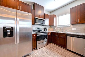 A modern kitchen with stainless steel appliances, wooden cabinets, and a granite countertop. - Modern Cozy 2BR Near Downtown Houston + Parking (Houston)
