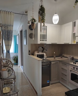 A kitchen with white cabinets, a microwave, a sink, and a hanging light fixture. - Dalhia's House: stunning gulf and mountain views, Wi-Fi, A/C Free parking (Cala Gonone)