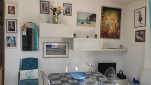 A dining area with a table set for two, a chair, a vase with flowers, and various framed artworks on the walls. - Dalhia's House: stunning gulf and mountain views, Wi-Fi, A/C Free parking (Cala Gonone)