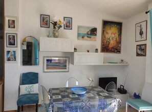 A dining area with a table set for two, a chair, a vase with flowers, and various framed artworks on the walls. - Dalhia's House: stunning gulf and mountain views, Wi-Fi, A/C Free parking (Cala Gonone)