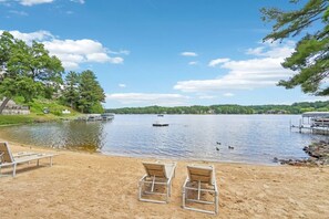 A lakeside view with a sandy beach, lounge chairs, and a dock with a boat. - Suzanne`s Beachfront Penthouse (Wisconsin Dells)