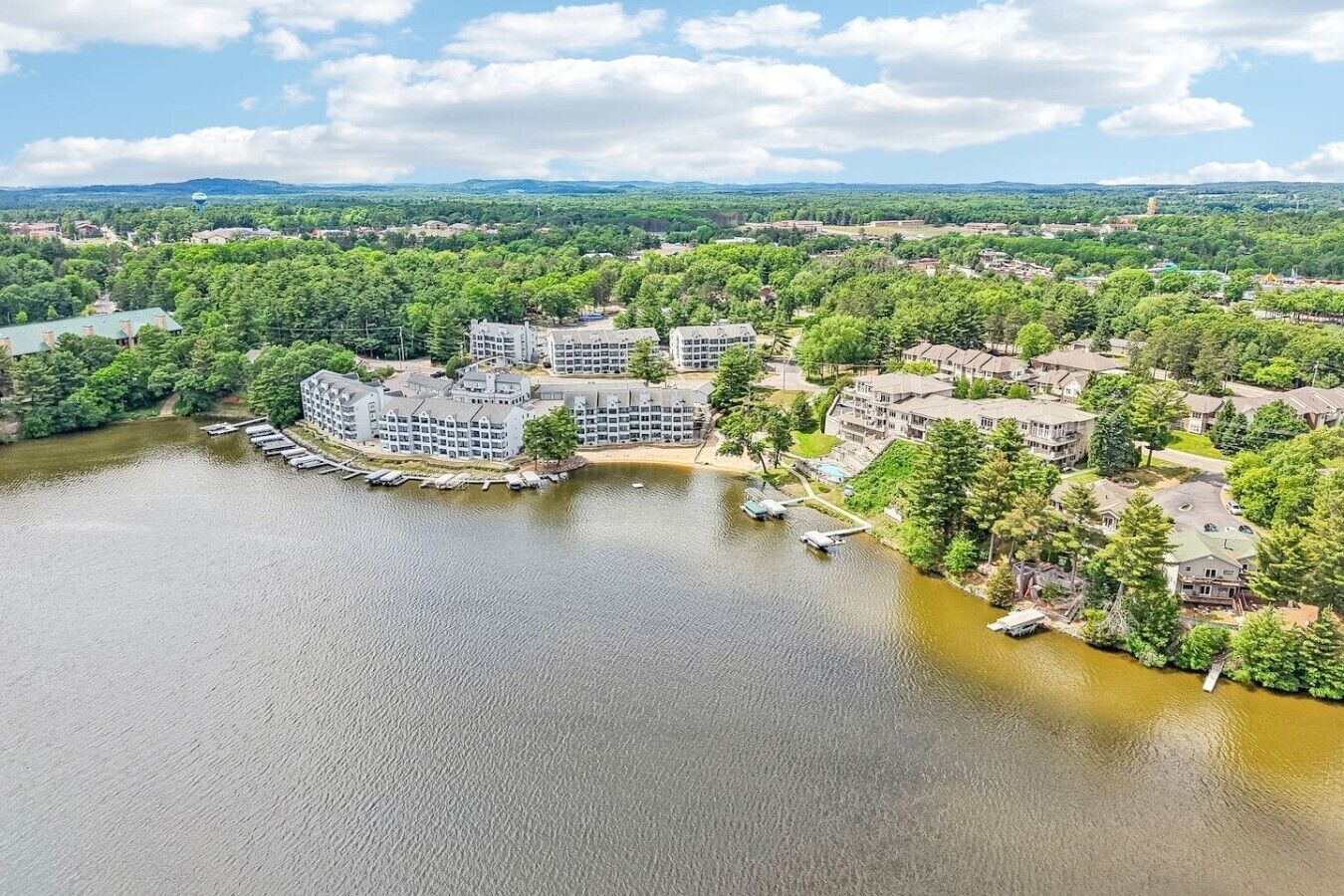 A lakeside hotel with multiple buildings, docked boats, and surrounding greenery.