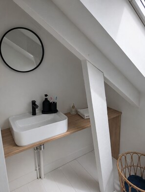 A modern bathroom with a white sink, a mirror, and a wooden shelf. - Charming house 500 m from the beach - Kerroc'h (Ploemeur)