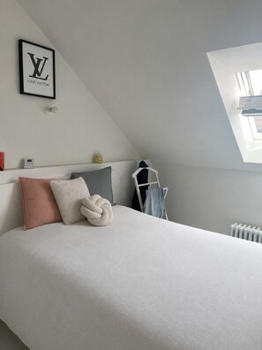 Un dormitorio con cama, logotipo de Louis Vuitton enmarcado, tragaluz, radiador y escalera.