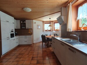 A kitchen with white cabinets, a tiled floor, a dining table with chairs, and a window with curtains. - Time out in the mountains, House Regina, 89sqm, 2-4 pers. Garden, terrace, KönigsCard (Pfronten)