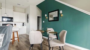 Een moderne keuken met witte kasten, een zwarte magnetron, en een eethoek met een ronde glazen tafel en vier stoelen.