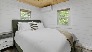 Ein Schlafzimmer mit einem Bett, zwei Fenstern, einem Nachttisch und einer Kommode.