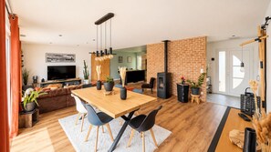 Ein moderner Wohnraum mit einem Holzesstisch, schwarzen Stühlen, einer Couch, einem Fernseher und einer Ziegelwand.
