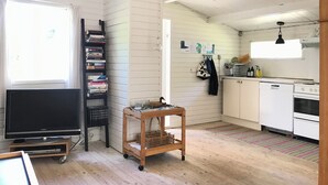 A compact living space with a TV, bookshelf, wooden cart, kitchen area, and a window. - Charming 2-bedroom cottage in Kulhuse, with a wonderful garden, close the beach (Kulhuse)