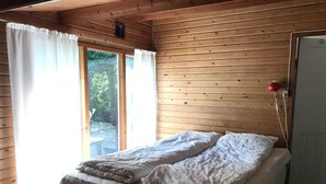 A wooden cabin room with a bed, a window with curtains, and a door. - Charming 2-bedroom cottage in Kulhuse, with a wonderful garden, close the beach (Kulhuse)