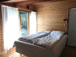Une pièce de cabane en bois comprenant un lit, une fenêtre avec des rideaux et une porte.