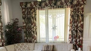 Ein Wohnzimmer mit Ecksofa, einer Kristallleuchter und blumigen Vorhängen.