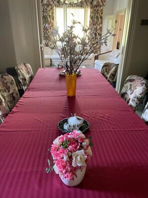 Una mesa de comedor con mantel rojo, un jarrón con flores rosa y blancas, y una tetera sobre una bandeja.