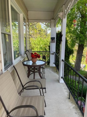A covered porch with a table and chairs, a potted plant, and a railing.