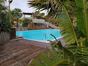 A swimming pool with a wooden deck, surrounded by tropical plants and a covered area. - Mobile home for rent at the Plage de Pampelonne St. Tropez-Ramatuelle (Saint-Tropez)
