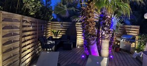 A wooden deck with outdoor furniture, a grill, and a palm tree. - Mobile home for rent at the Plage de Pampelonne St. Tropez-Ramatuelle (Saint-Tropez)