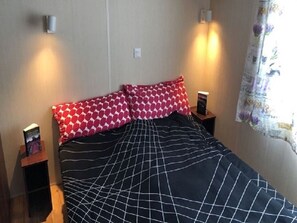A bed with a patterned bedspread, two bedside tables, and a wall-mounted light fixture. - Mobile home for rent at the Plage de Pampelonne St. Tropez-Ramatuelle (Saint-Tropez)