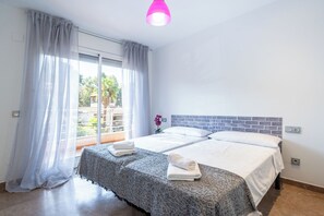 Une chambre d’hôtel avec deux lits, un balcon, un luminaire suspendu rose et une vue sur la verdure environnante.