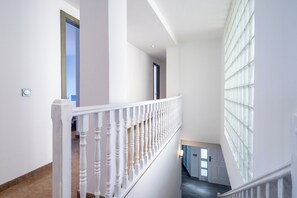 Un escalier avec des balustrades blanches menant à un palier où se trouvent une porte et une grande fenêtre.