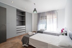 Un dormitorio con dos camas, un armario y una ventana con cortinas traslúcidas.