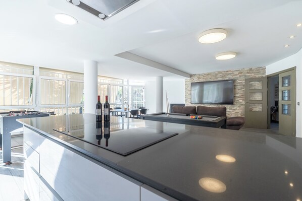 A modern kitchen with a foosball table, a pool table, and a flat-screen TV mounted on a stone wall.