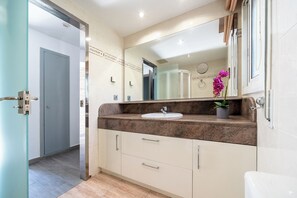 Un baño con lavamanos, espejo y planta en maceta.