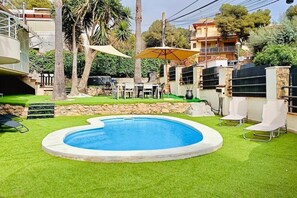 A swimming pool with artificial grass, a sun umbrella, and white chairs.