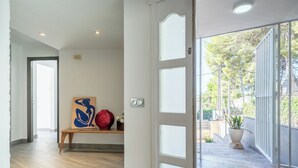 Un couloir avec un banc en bois, un vase rouge et un tableau abstrait bleu.