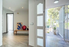 A hallway with a wooden bench, a red vase, and a blue abstract painting.