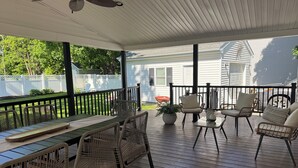 Eine überdachte Veranda mit Tisch und Stühlen, einem Deckenventilator und Blick auf ein Haus und Garten.