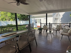 A covered porch with a table and chairs, a ceiling fan, and a view of a house and yard. - Central Wakefield Home with Spacious Outdoor Living and AC (South Kingstown)