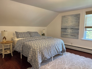 A bedroom with a bed, bedside tables, a window, and a wall-mounted artwork. - Central Wakefield Home with Spacious Outdoor Living and AC (South Kingstown)