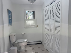 A bathroom with a toilet, a window, a heater, and a white closet. - Central Wakefield Home with Spacious Outdoor Living and AC (South Kingstown)