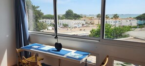 Ein Zimmer mit großem Fenster und Blick auf die Küste, einem Schreibtisch mit Papieren sowie einem hängenden Gegenstand.