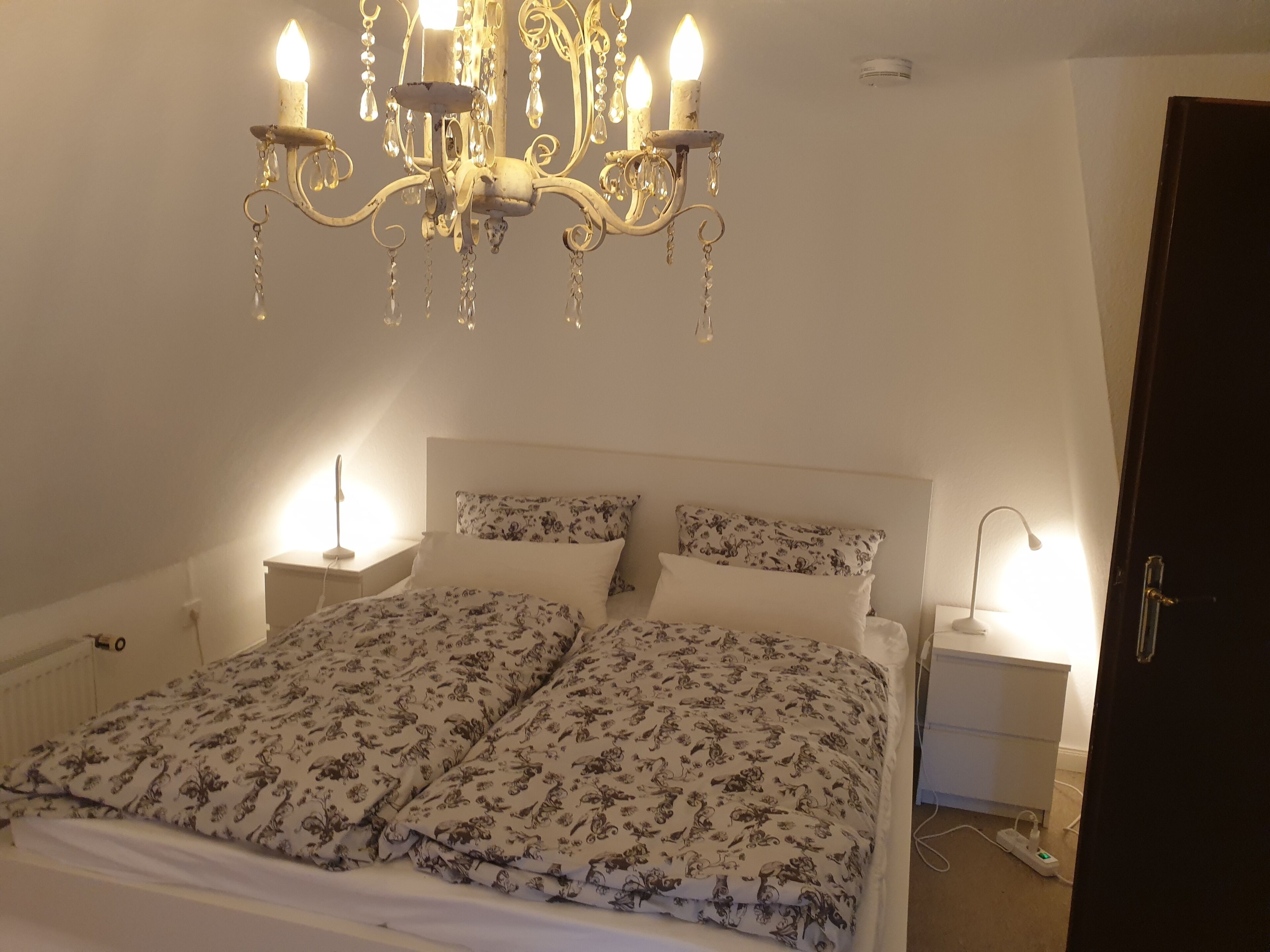 Ein Schlafzimmer mit einem Bett, zwei Nachttischen, einer Deckenleuchte und einer Tür.