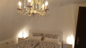 A bedroom with a bed, two bedside tables, a chandelier, and a door.