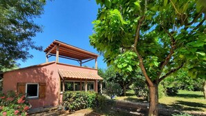 Una casa rústica con tejado de baldosas, un porche cubierto y un jardín con diversas plantas y un árbol.