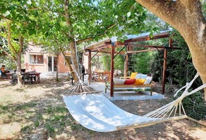 A hammock under a wooden pergola, a wooden bench with cushions, and a dining table with chairs in a garden setting. - A quiet home in a little slice of paradise - Pétanque court (Roquebrune-sur-Argens)