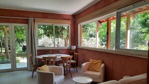 Una habitación con sofá, sillas, una mesa de comedor y vistas a zonas verdes a través de amplias ventanas.