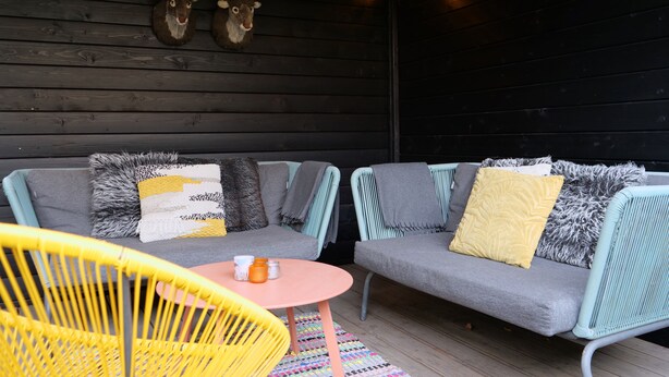 A cozy outdoor seating area with a sofa and chairs, wooden walls, and decorative antlers.